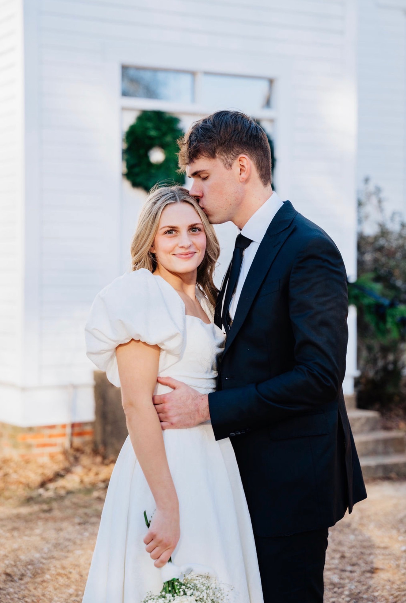 Bride and groom outside white chapel, groom in navy suit